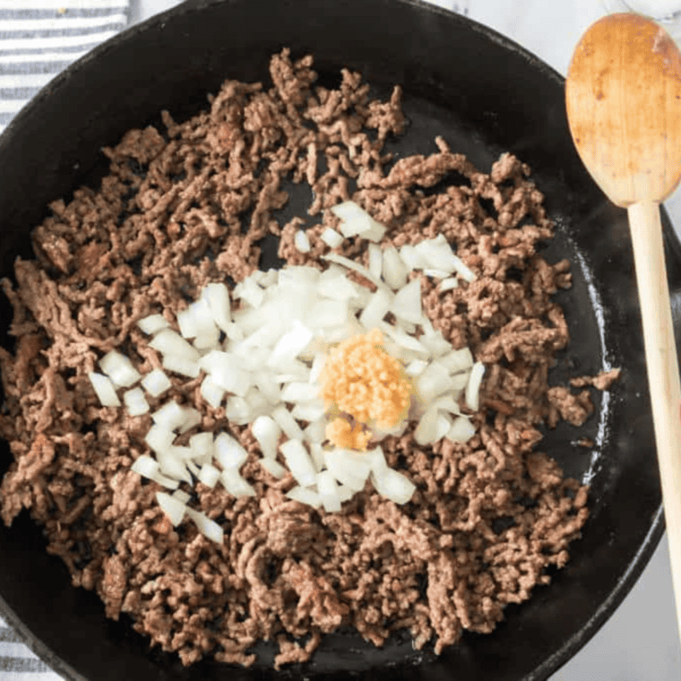 Ground beef browning in a skillet with diced onion and garlic