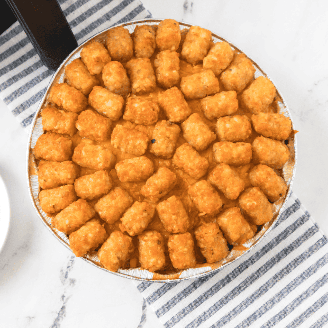 Frozen tater tots arranged in a single layer over cowboy casserole before air frying