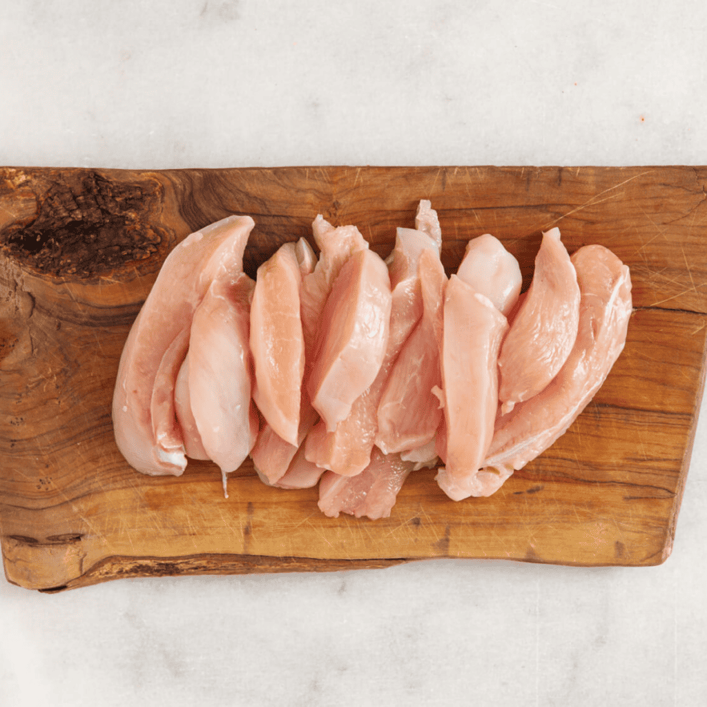 Ingredients for Honey Garlic Chicken Tenders: Raw chicken tenders arranged on a wooden cutting board, showcasing the main ingredient for the recipe.