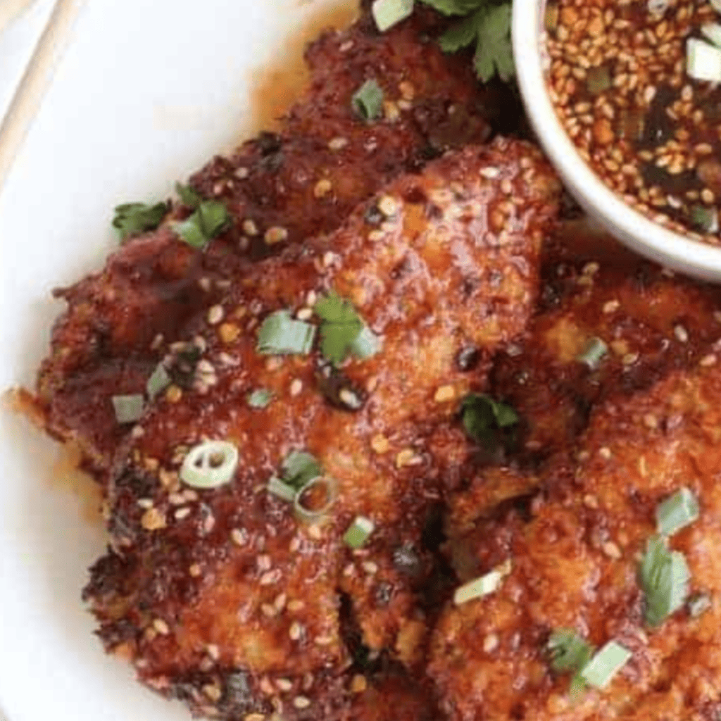 Golden brown air fryer honey garlic chicken tenders on a plate with a side of dipping sauce.
