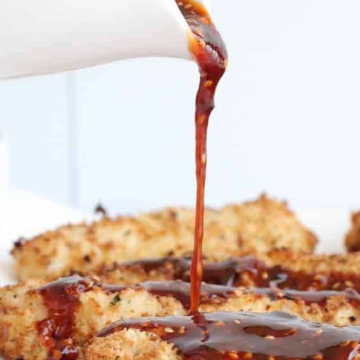 Drizzling extra honey garlic sauce over the cooked chicken tenders for added flavor.