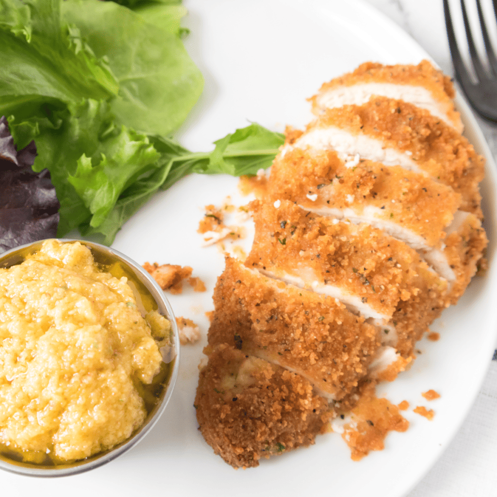 Air fryer Parmesan crusted chicken topped with melted cheese and golden breadcrumb crust served on a white plate.