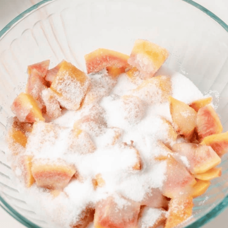 Fresh peaches being washed, peeled, sliced, and diced in a bowl with granulated sugar, ready to release juice.