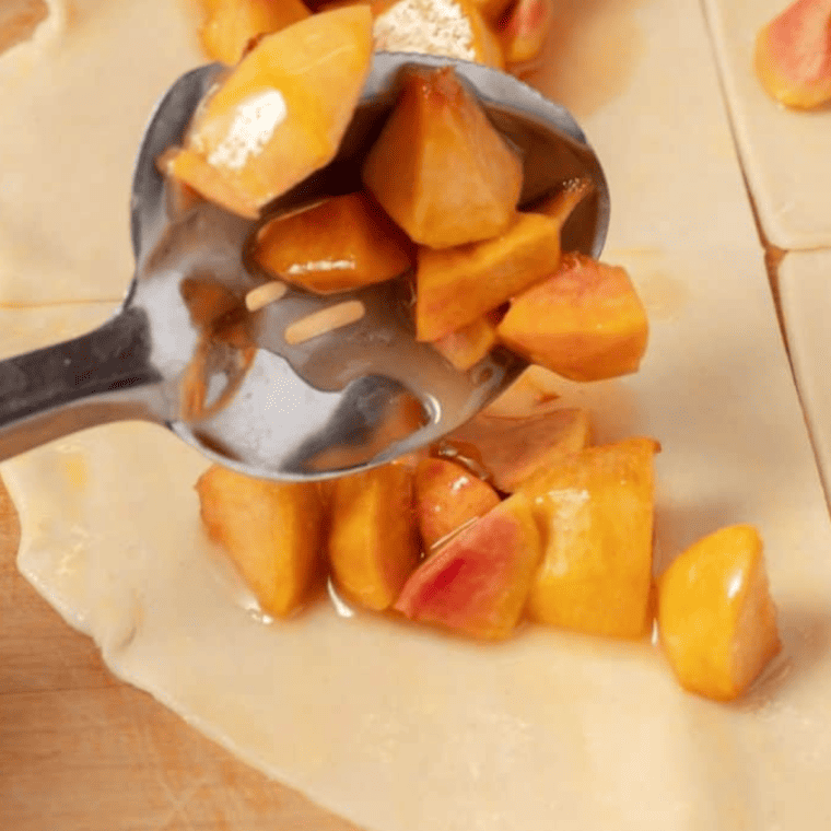 Pastry brush applying egg wash to pie dough, then adding homemade peach pie filling to dough section.