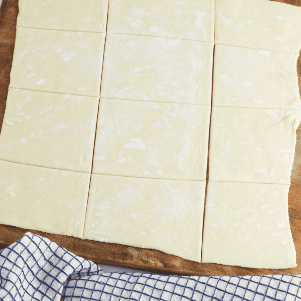 Puff pastry rolled out on a floured surface and cut into 2x2-inch squares, ready to be filled and air-fried..