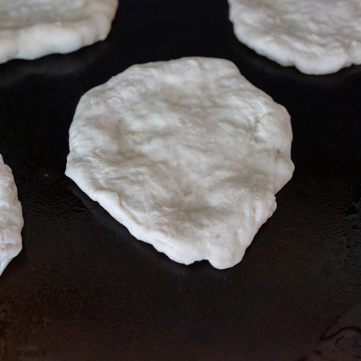 Blackstone griddle preheated and oiled, with naan dough cooking until golden brown on both sides