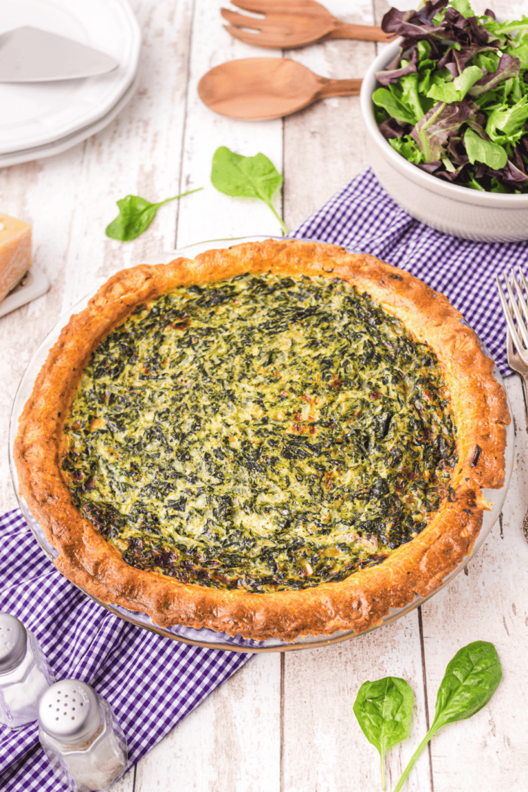 Spinach quiche sliced on a plate showing creamy egg filling with spinach and melted cheese in a golden crust.
