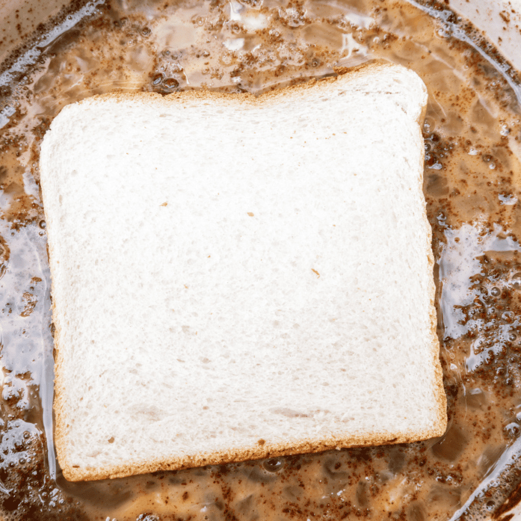 Bread slices being dipped and coated evenly in egg mixture for French toast.