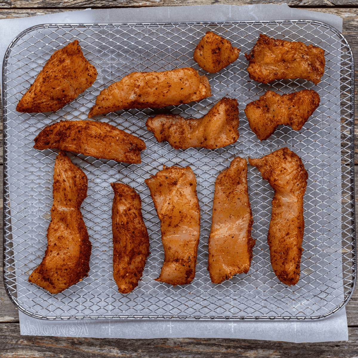 Seasoned chicken pieces in a single layer in the air fryer basket before cooking
