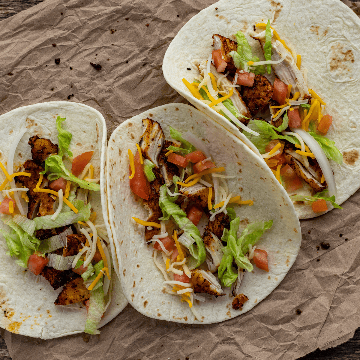 Three air fryer chicken street tacos on corn tortillas topped with onion, cilantro, and lime