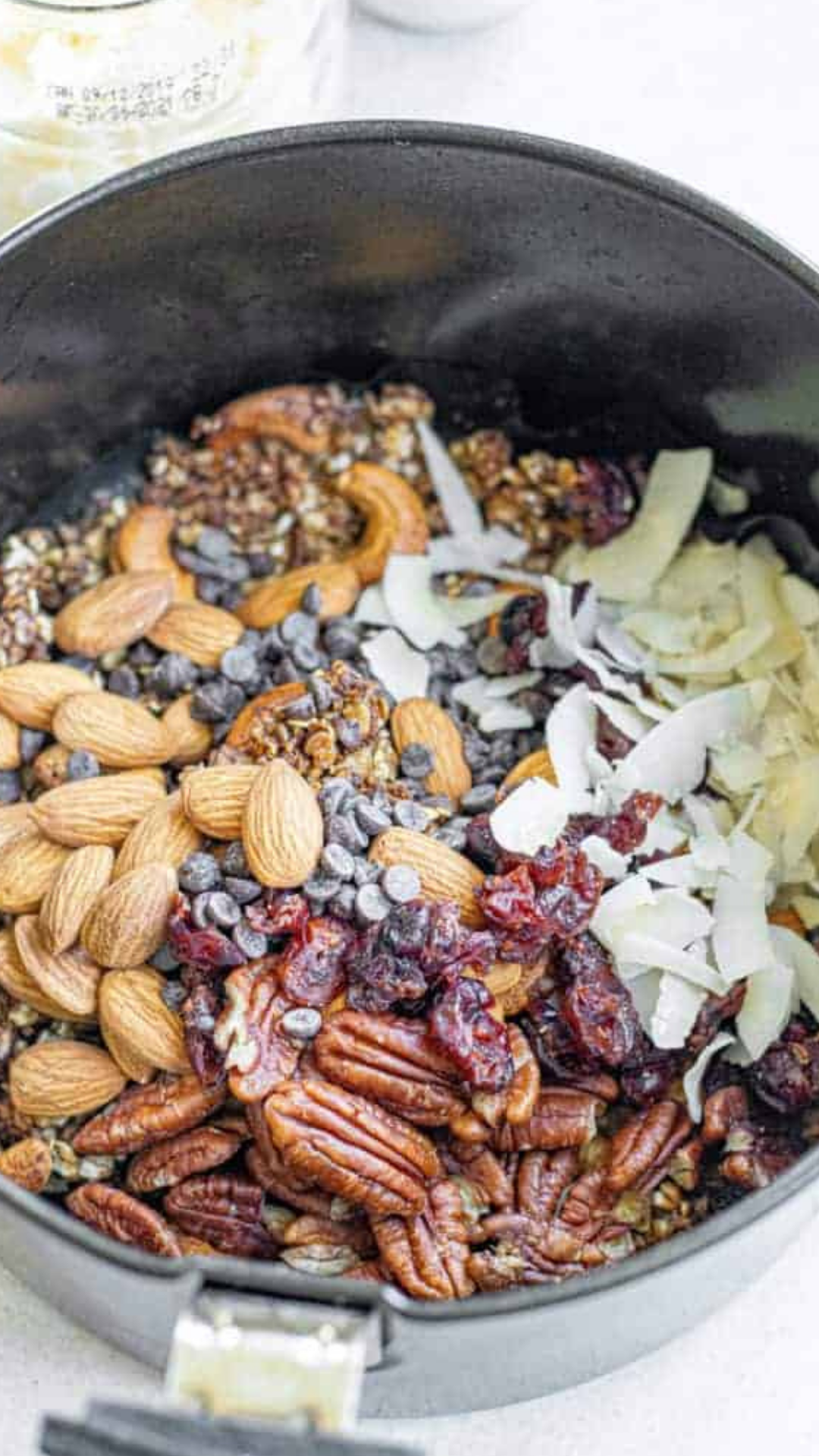Uncooked granola spread in an even layer in a parchment-lined air fryer basket