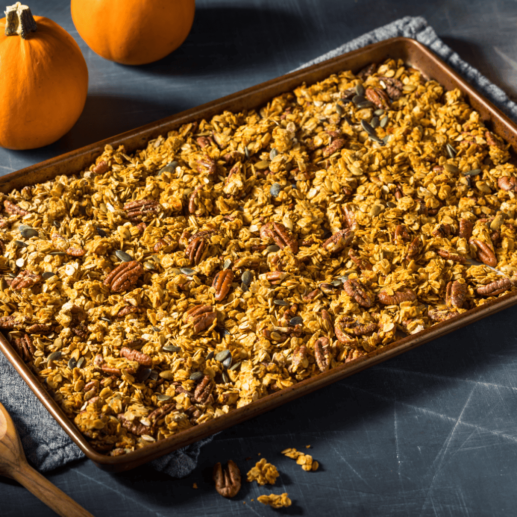 Homemade pumpkin spice granola on a tray with mini pumpkins in the background