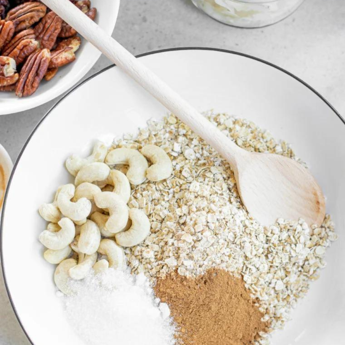Rolled oats, chopped nuts, and pumpkin seeds mixed in a large white bowl