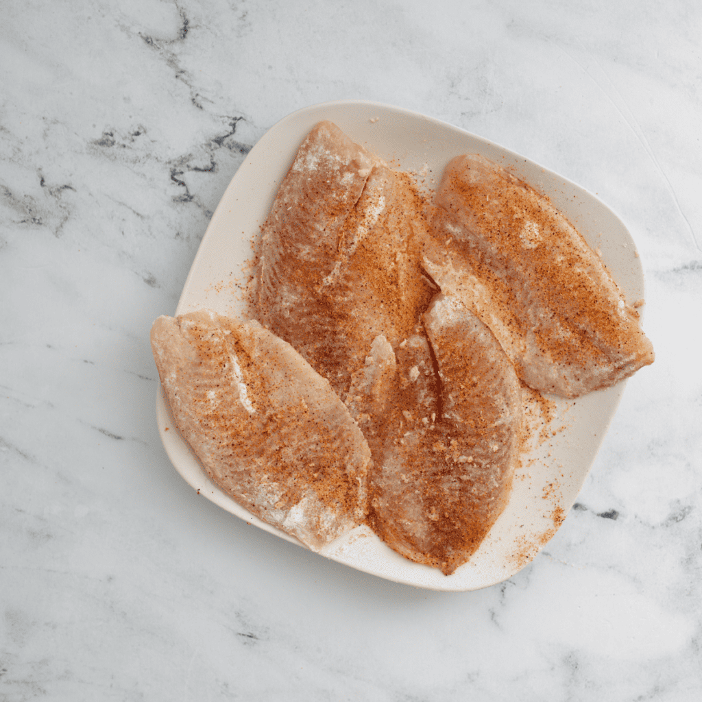 Catfish fillets being dredged in Cajun seasoning before griddling