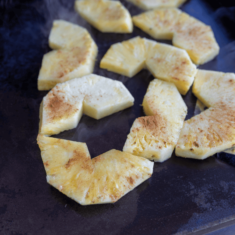 Pineapple slices cooking on a Blackstone griddle with caramelized grill marks.