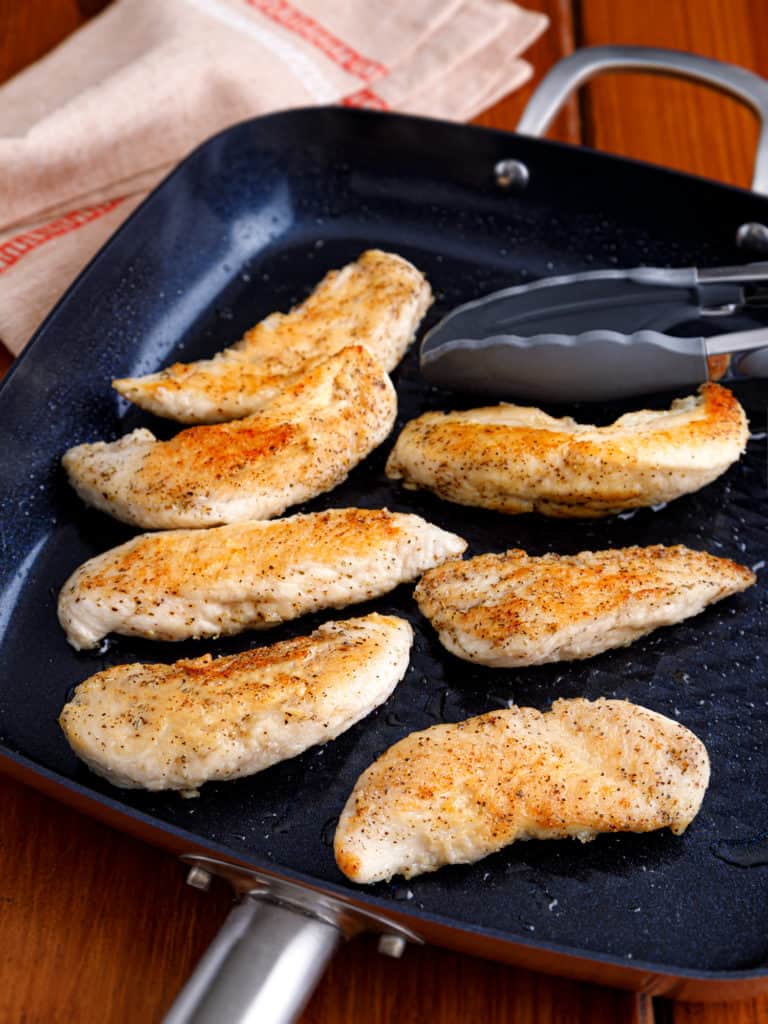 Boneless chicken breasts seasoned and cooking in a skillet until golden brown for Chicken Marsala.