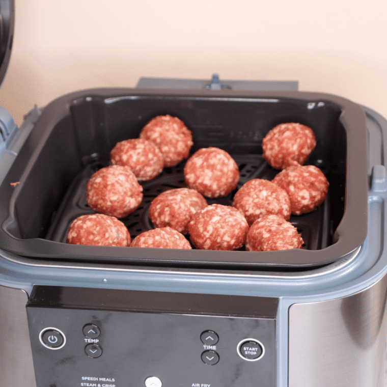 Meatballs arranged in a single layer on Ninja Speedi crisper tray above pasta, ready for SteamCrisp cooking with lid closed.
