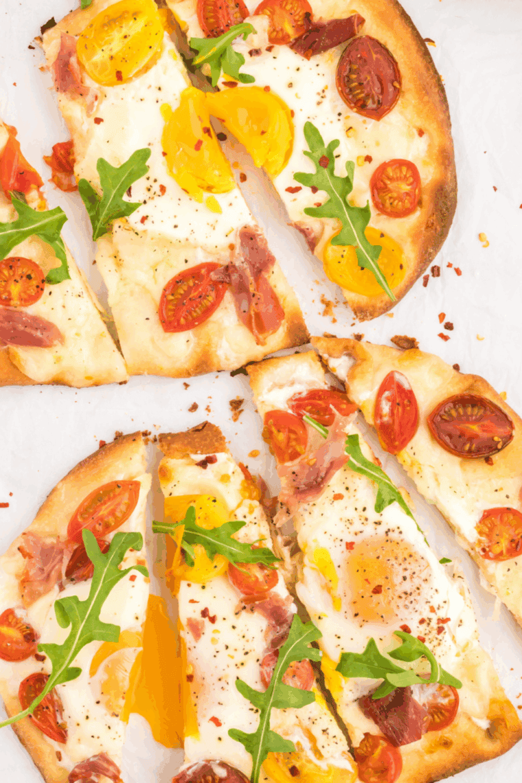Crispy air fryer breakfast flatbread pizza topped with melted mozzarella, scrambled eggs, crispy bacon bits, and fresh chives on a wooden cutting board.