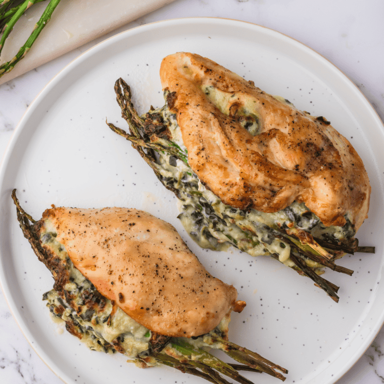 Two artichoke dip stuffed chicken breasts on a white plate garnished with fresh parsley