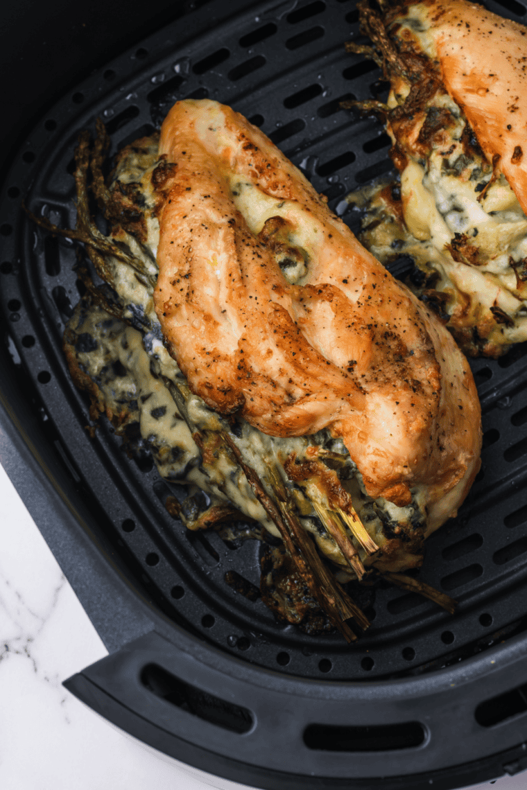 Sliced air fryer chicken stuffed with artichoke dip showing the cheesy spinach center