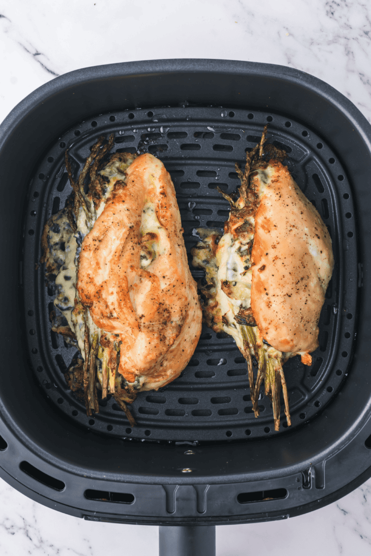 Cooked artichoke stuffed chicken resting on a cutting board before slicing