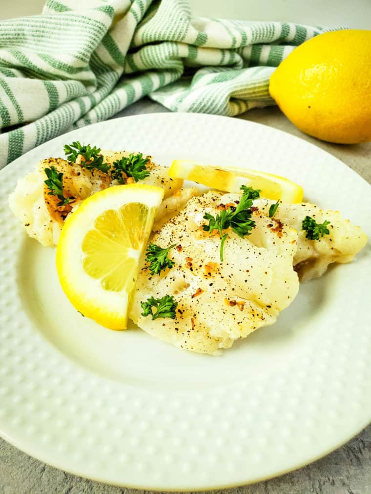 Air Fryer Lemon Pepper Cod fillets with a crispy crust, garnished with fresh lemon slices and pepper."