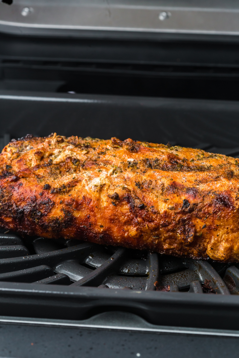 Frozen pork tenderloin cooking in an air fryer, golden and seasoned.