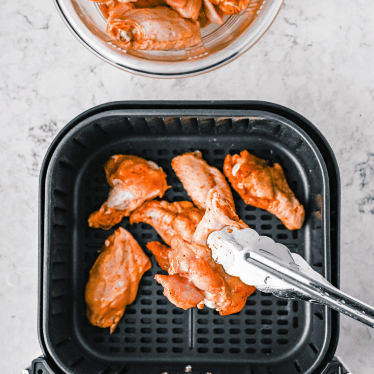 Arranging seasoned chicken wings in the air fryer basket for cooking.