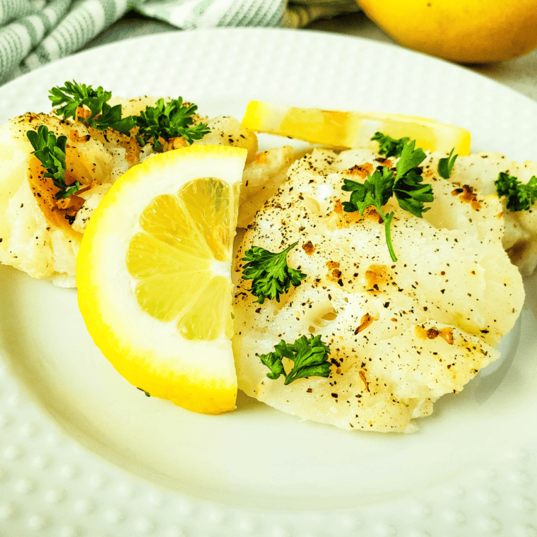 Air Fryer Lemon Pepper Cod fillets with a crispy, golden crust and garnished with lemon wedges.