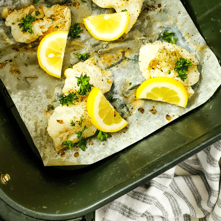 Air Fryer Lemon Pepper Cod fillets with a crispy golden crust, garnished with lemon wedges and herbs.