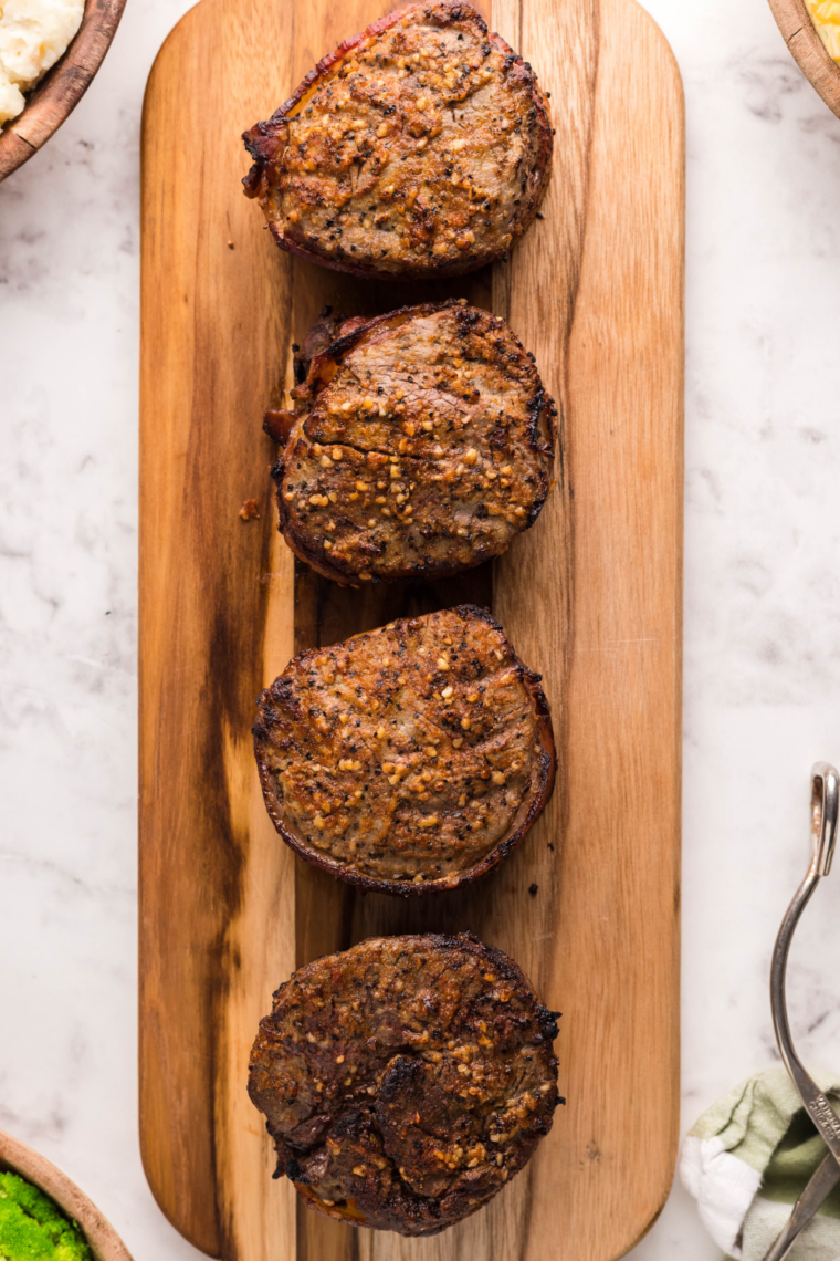 Filet mignon steaks sizzling on a flat top Blackstone grill with a golden crust forming