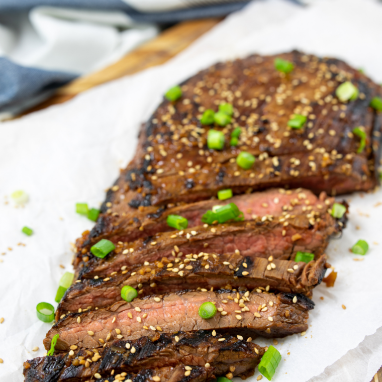 Raw flank steak seasoned with salt, pepper, and oil placed on a preheated Blackstone griddle.