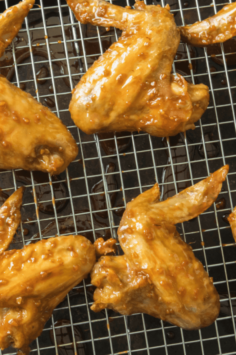 Crispy chicken wings coated in spicy garlic sauce served on a plate with dipping sauce and garnish.