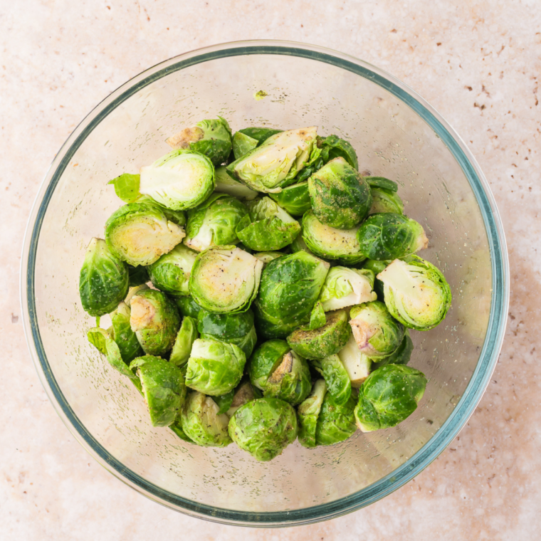 Halved Brussels sprouts tossed with olive oil, salt, pepper, and garlic powder in a bowl