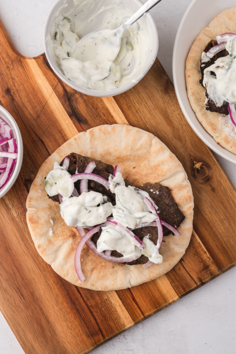 Air fried Trader Joe's gyro slices piled on a white plate with tzatziki and lemon wedges alongside
