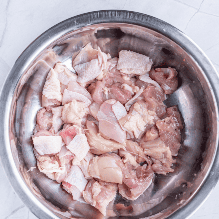Raw chicken thighs cut into bite-sized chunks with skin on and trimmed fat prepared for air fryer karaage.
