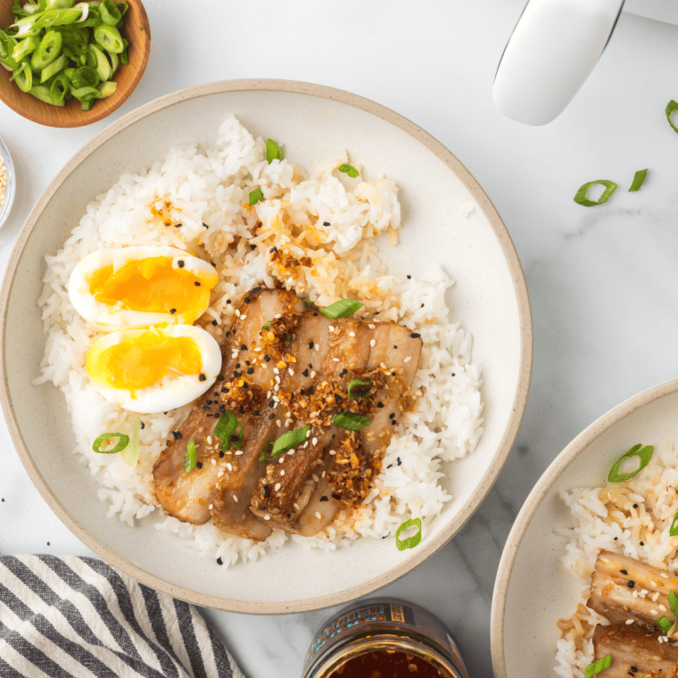 Air Fryer Pork Belly Rice Bowl - A close-up view of a delicious rice bowl topped with crispy air-fried pork belly, garnished with green onions and sesame seeds.