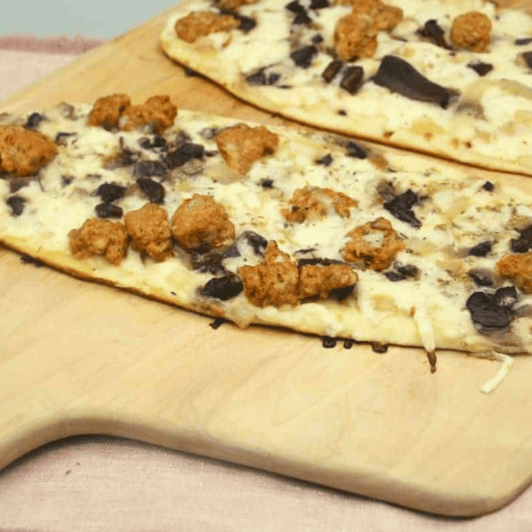 Blackstone griddle flatbread pizza topped with sausage, mushrooms, and melted cheese.