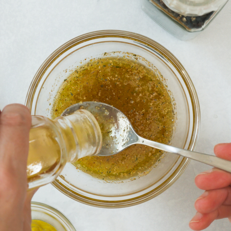 Whisking mayonnaise, anchovy paste and garlic into Caesar dressing in a glass bowl