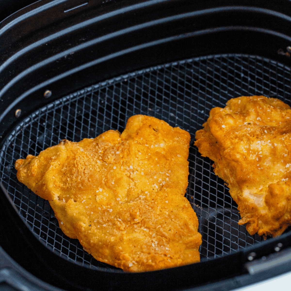 Crispy reheated fish and chips in air fryer basket.