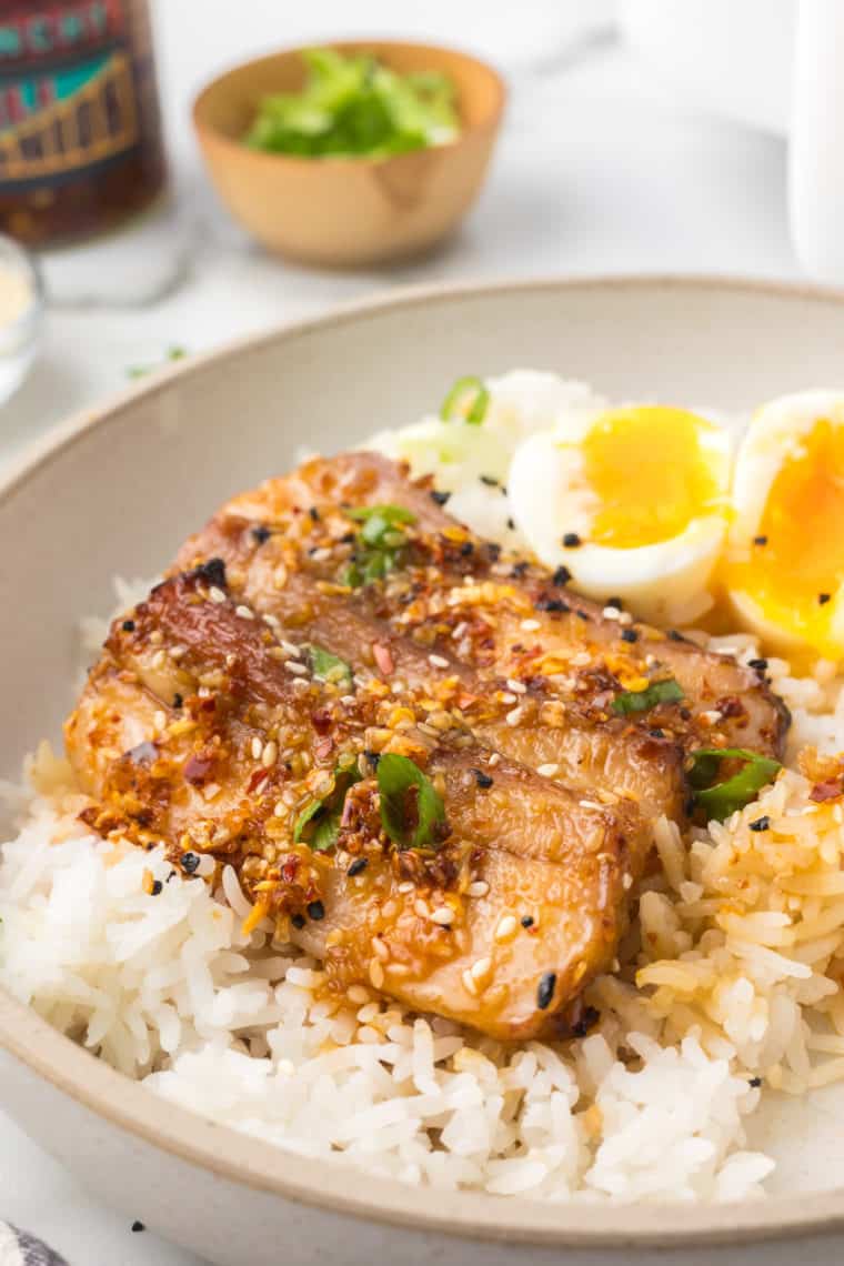 A delicious Trader Joe's Air Fryer Pork Belly Rice Bowl featuring crispy pork belly over fluffy rice, garnished with fresh vegetables and drizzled with sauce.