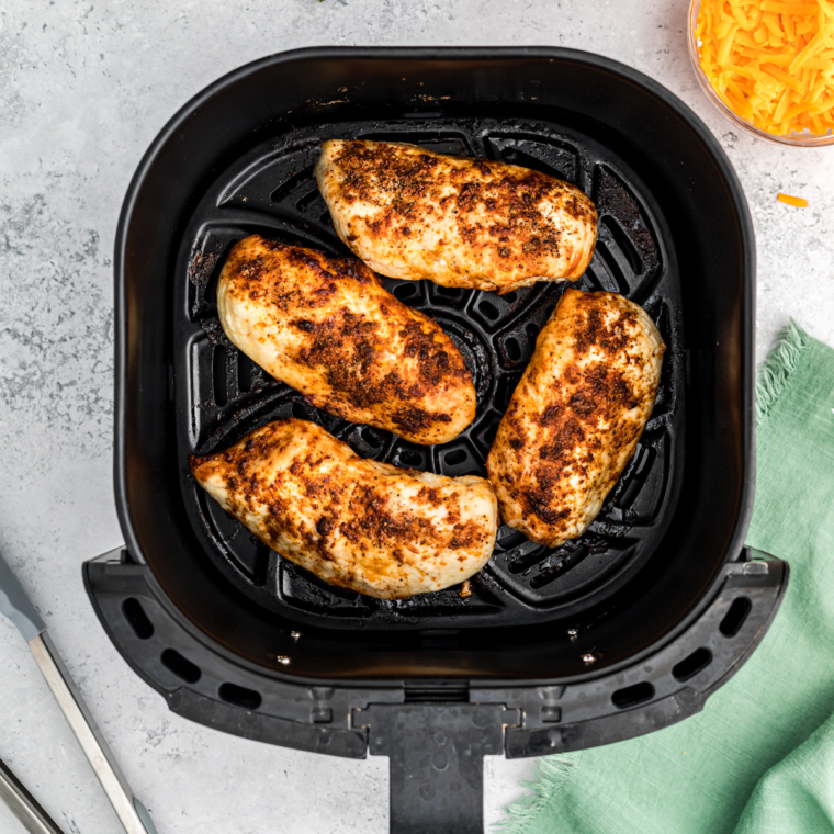 Chicken breasts placed in the air fryer basket, coated in salsa and seasonings, cooking to juicy perfection.