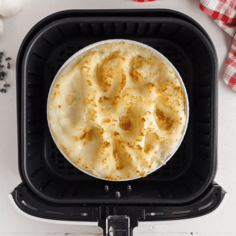 Mashed potatoes spread over meat filling with butter pieces on top, baking until golden in air fryer