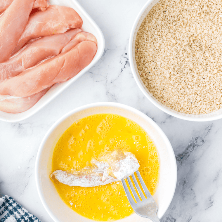 Chicken strips being coated in flour, dipped in egg wash, and covered with panko breadcrumbs.