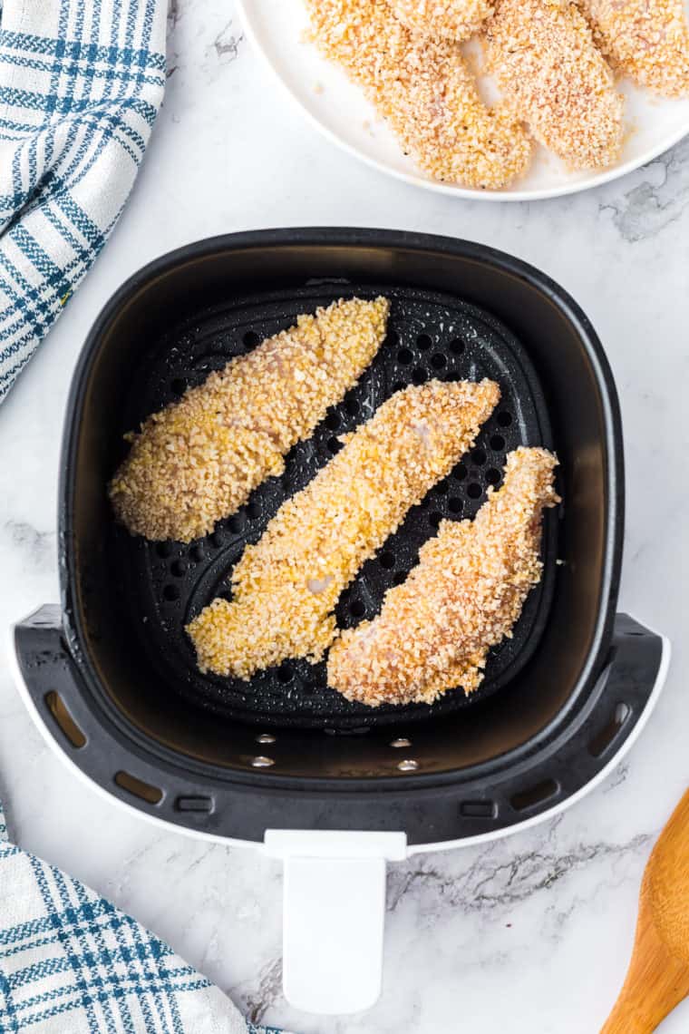 Air fryer basket sprayed with cooking spray, ready for breaded chicken strips.