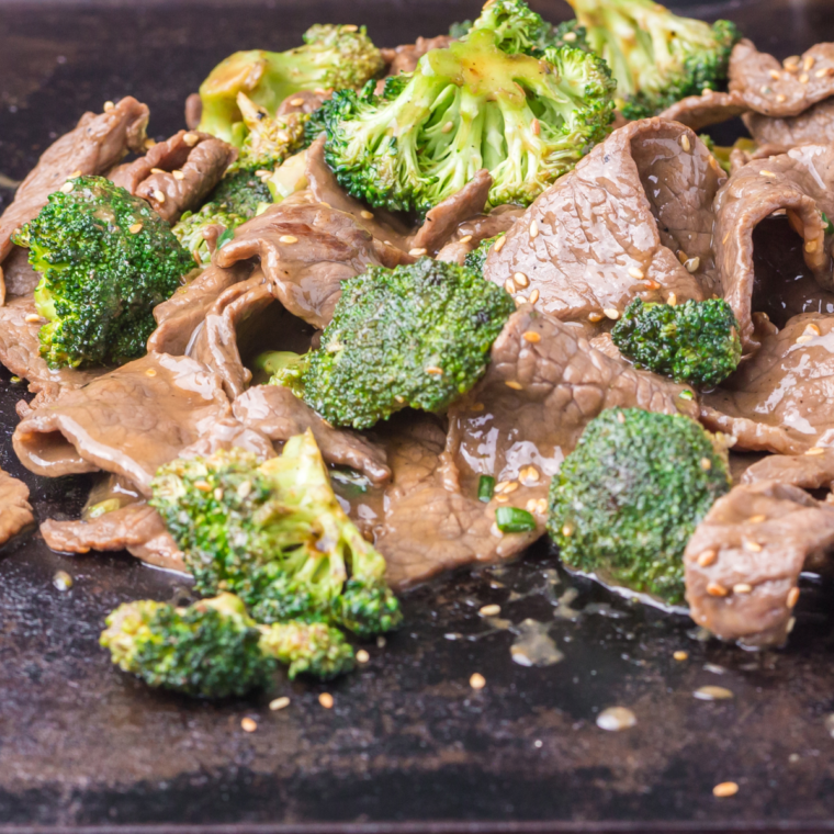 Close-up of beef and broccoli cooking on a Blackstone griddle with garlic sauce coating the ingredients.