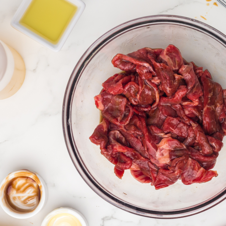 Thinly sliced beef tossed in savory sauce marinade in a bowl for Blackstone beef and broccoli, soaking up flavor before cooking.