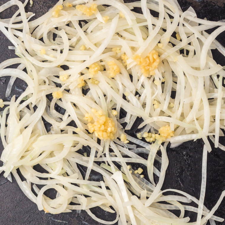 Sliced onions and garlic caramelizing in butter on a Blackstone griddle