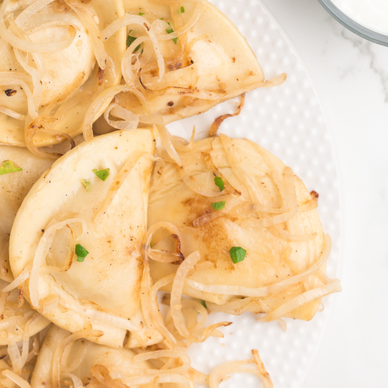 Golden-brown pierogies cooking on a Blackstone griddle with caramelized onions, ready to serve.