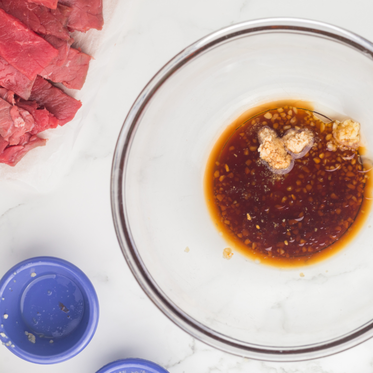 Thinly sliced raw steak strips on a cutting board ready for the griddle